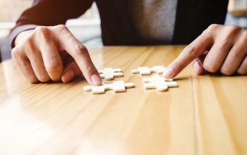 Female hands on a wooden office desk pick puzzle.Business solutions, success and strategy concept. Businessman hand connecting jigsaw puzzle.Close up photo with small dof